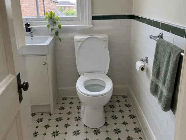 Clean white toilet in a tiled bathroom with a sink and towel rail in Stanmore